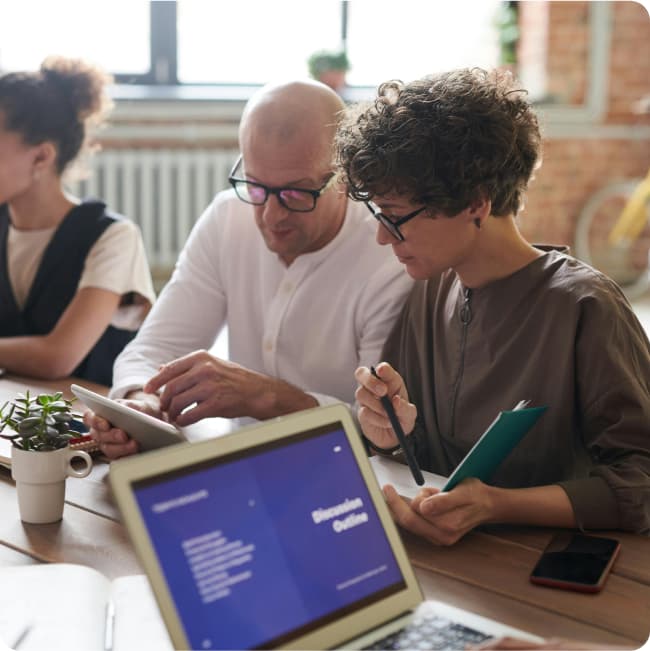 Stock photo of two women and a man around a table where the man and one of the women are collaborating using their paper notebooks