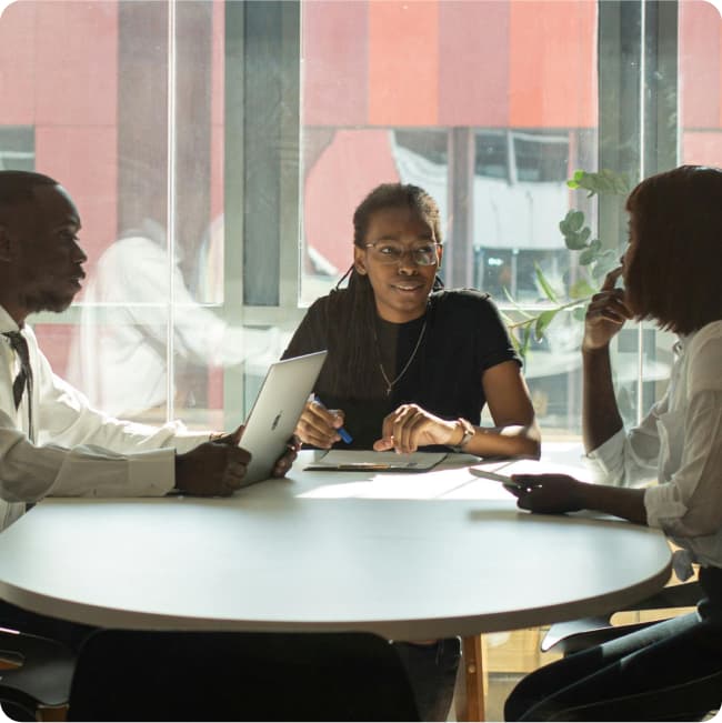 Stock photo of two women and a man collaborating around a table using their paper and electronic notebooks